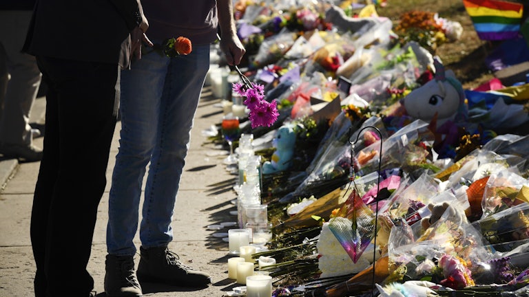Two people stand holding flowers in front of a pile of flowers and candles.