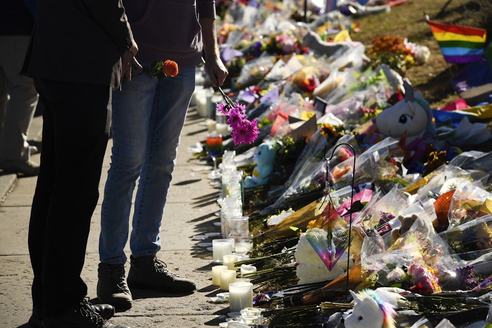 Two people stand holding flowers in front of a pile of flowers and candles.