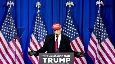 Donald Trump stands at a lectern in front of four American flags.