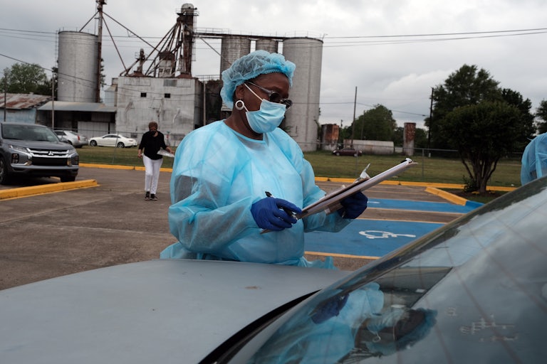 A medical worker in protective gear scans a clipboard at a drive-in vaccination clinic.