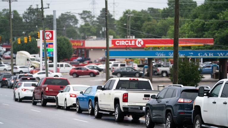Cars on the road wait in line to drive into a gas station.