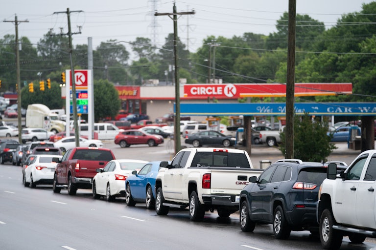 Cars on the road wait in line to drive into a gas station.