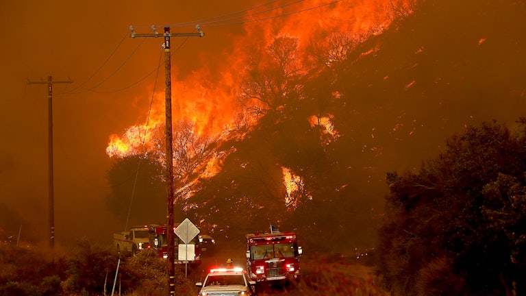 Emergency vehicles drive toward the camera with a fire in the background.