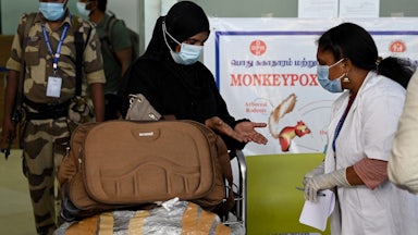 A health worker examines a woman's hands at an airport checkpoint.