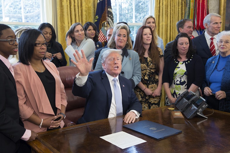 Former President Trump, surrounded by supporters in the Oval Office, signs an anti-sex trafficking bill