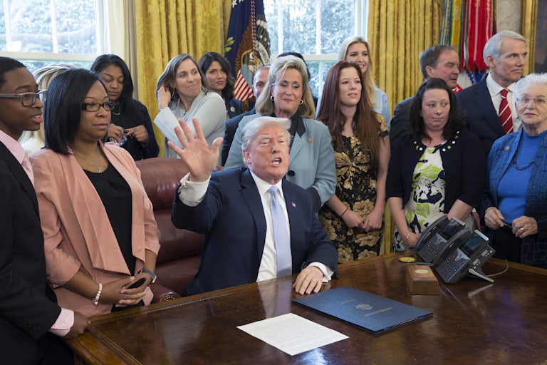 Former President Trump, surrounded by supporters in the Oval Office, signs an anti-sex trafficking bill
