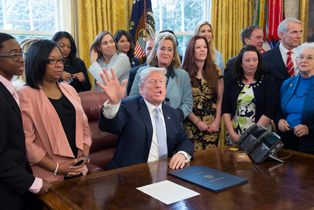 Former President Trump, surrounded by supporters in the Oval Office, signs an anti-sex trafficking bill
