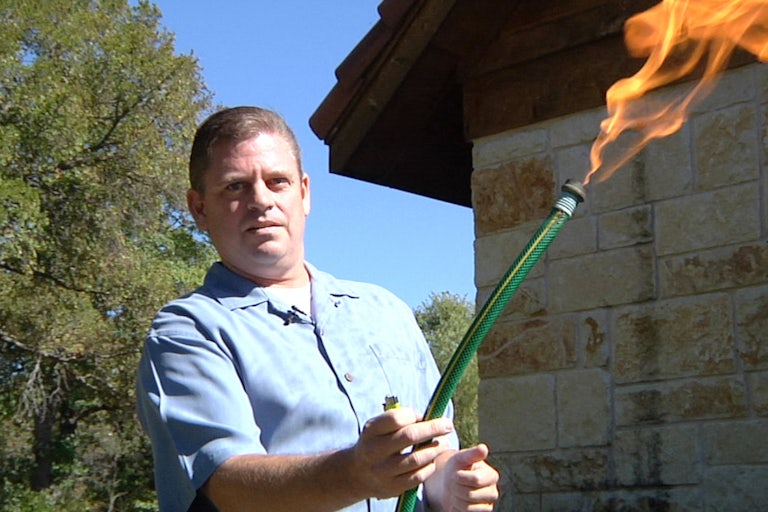 A man holds a garden hose with flames coming out of it.