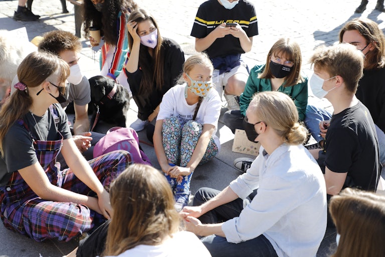 Young people sit, wearing facemasks, on the ground.
