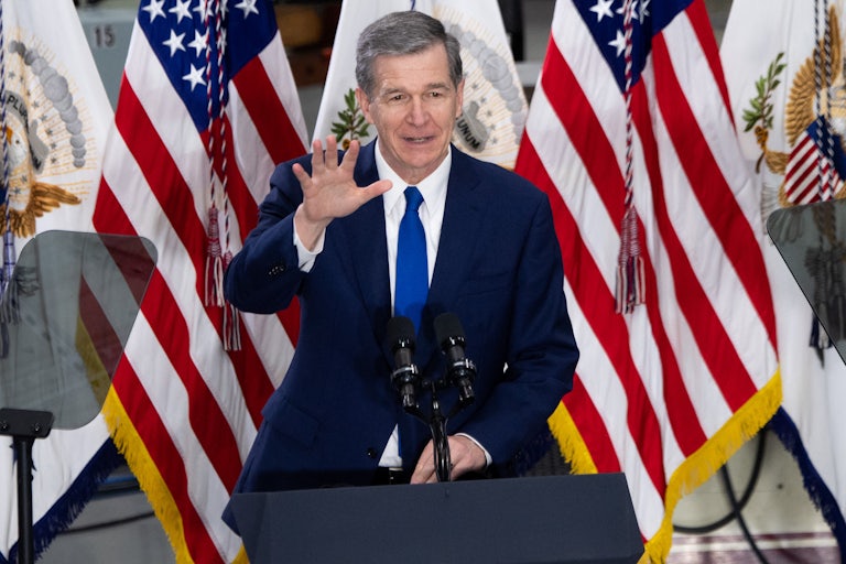 North Carolina Governor Roy Cooper stands behind a lectern waving.