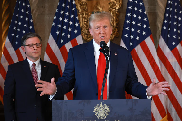 Mike Johnson stands behind Donald Trump as he speaks at a podium