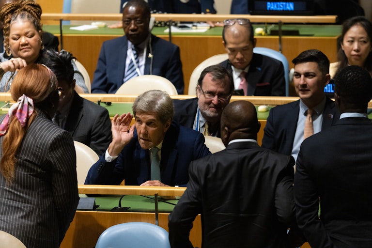 John Kerry leans forward to hear someone speaking to him.