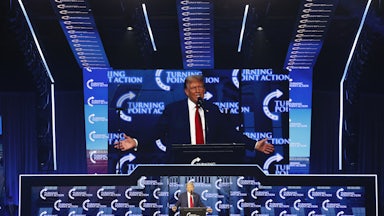 Donald Trump stands at a lectern while his image is projected above him.