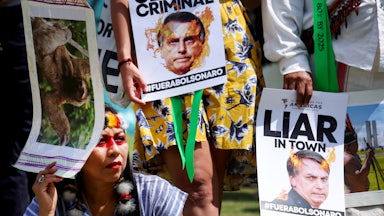 People hold signs calling Bolsonaro a "climate criminal" and a liar.