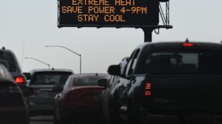 Cars sit in bumper-to-bumper traffic beneath a sign saying "Extreme Heat Save Power 4-9 PM Stay Cool."