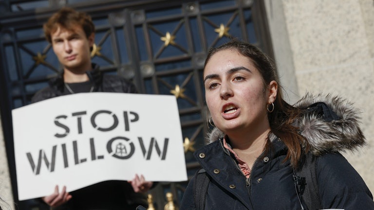 A student speaks with another, behind, holding a sign saying "Stop Willow."