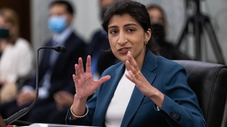 FTC Commissioner Lina M. Khan smiles and gestures with her hands while testifying during a Senate hearing