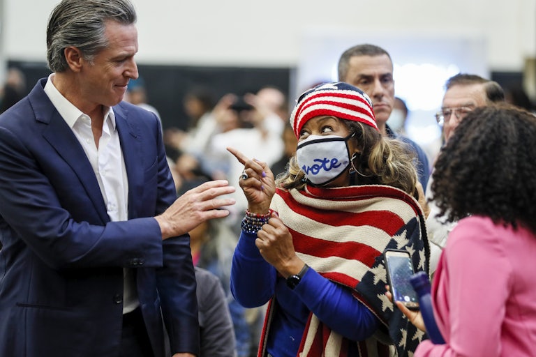 Gavin Newsom passes a woman clad in an American flag scarf, with a mask reading "vote."