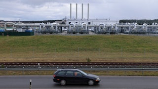 A car drives in front of a series of pipes and gears.