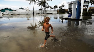 A child runs through standing water around a gas station.