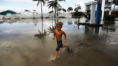 A child runs through standing water around a gas station.