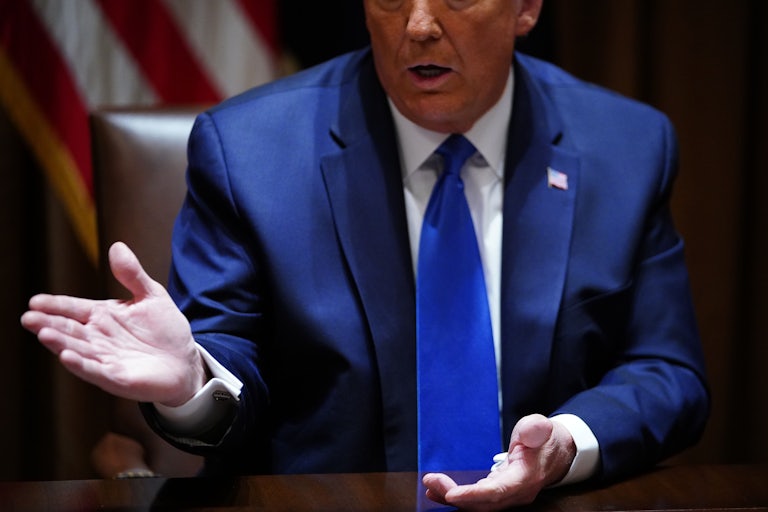 Donald Trump, sitting at a desk, gestures while he speaks 