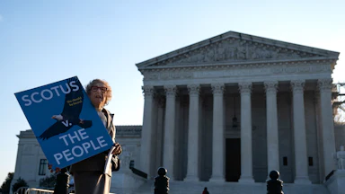 A woman holds a sign that reads "SCOTUS vs. the people" outside the Supreme Court.