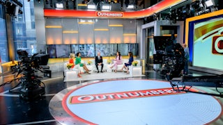 The set of the Fox News Outnumbered. The hosts sit with a guest on white armchairs arranged in a semicircle.