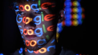 In this photo illustration, brightly colored Google logos are projected onto a man's face.