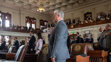 Representatives in suits stand with their hands over their hearts.