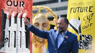 Ben Jealous raises his hand while standing at a microphone in front of posters.