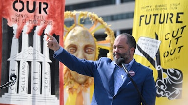 Ben Jealous raises his hand while standing at a microphone in front of posters.