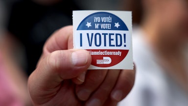 A hand holds an "I Voted" sticker.