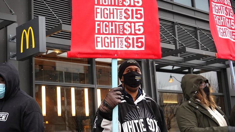 Three masked workers in front of a McDonalds holding red "Fight for 15" signs