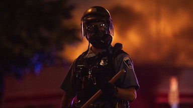 A police officer stands with a baton as a fire burns inside an Auto Zone store in Minneapolis