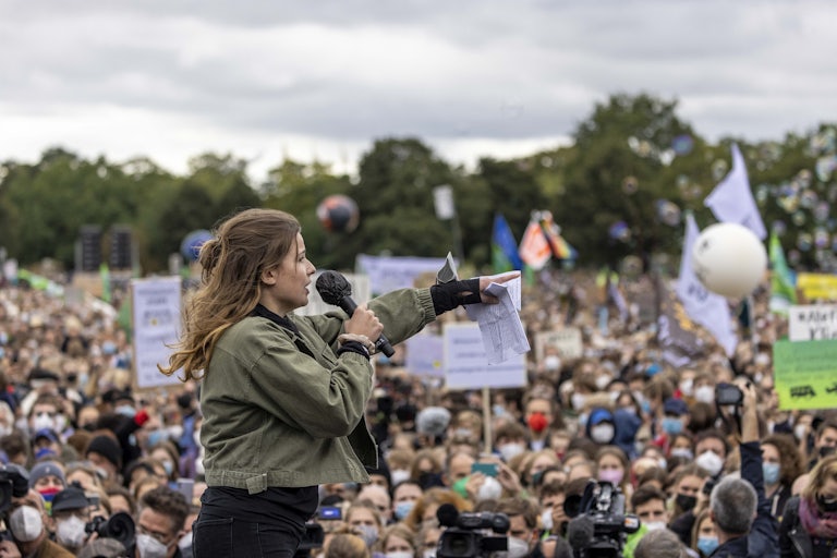 A woman speaking into a microphone points to the crowd.