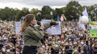 A woman speaking into a microphone points to the crowd.