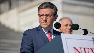 Mike Johnson looks to the side while standing at a podium