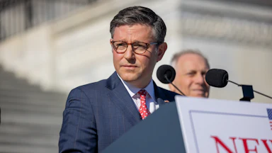 Mike Johnson looks to the side while standing at a podium