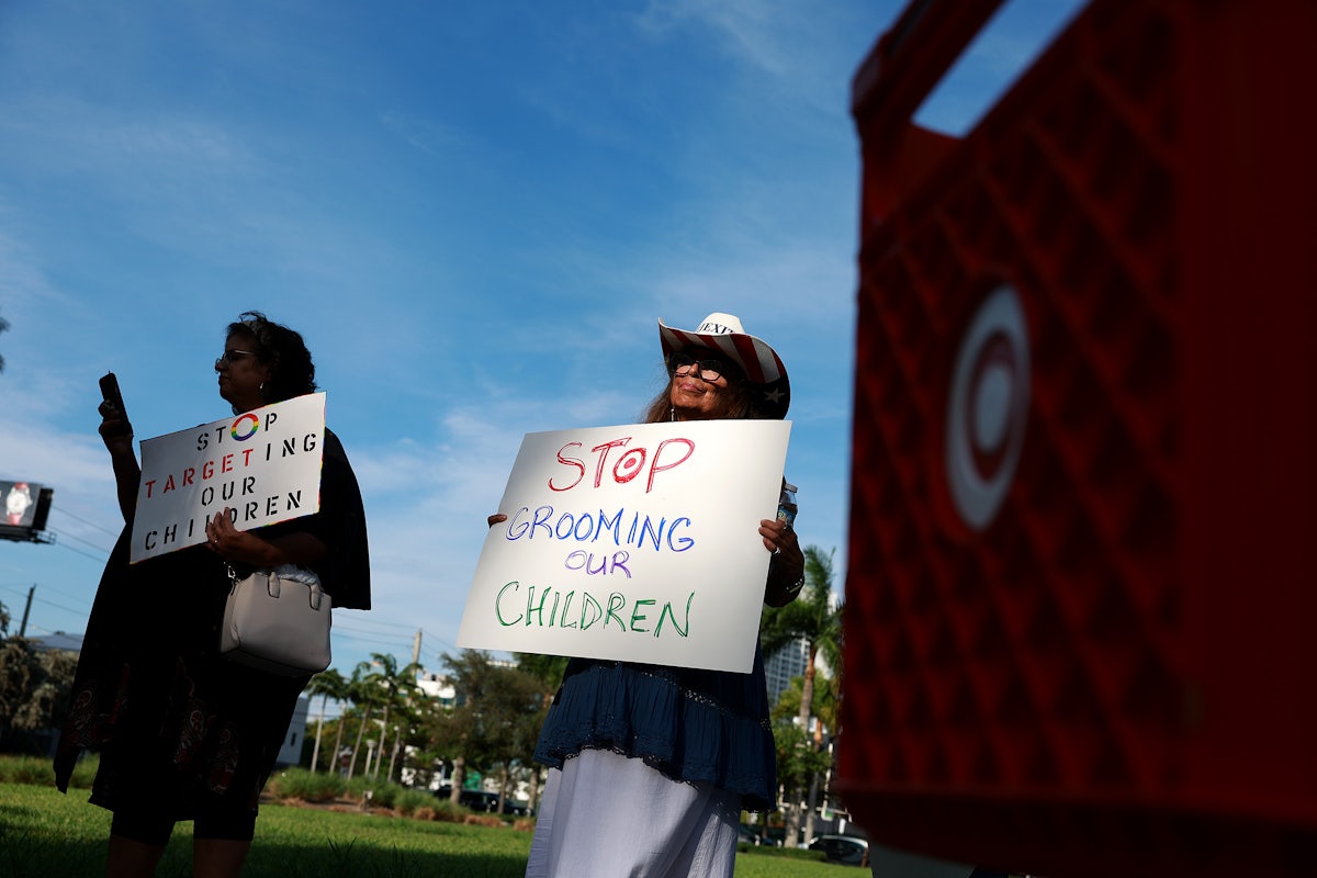 Two demonstrators stand next to a Target shopping cart holding anti-LGBTQ signs.