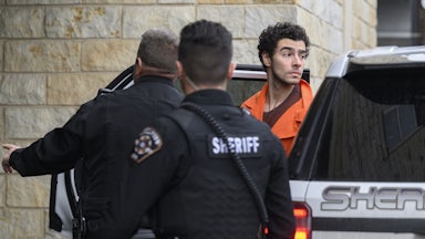 Luigi Mangione in an orange jumpsuit is led out of a car by several police officers