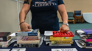 A woman rests her hands on stacks of books.