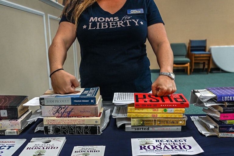 A woman rests her hands on stacks of books.