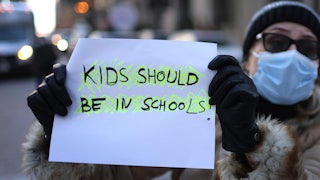 a masked person holding a sign that reads "kids should be in schools"