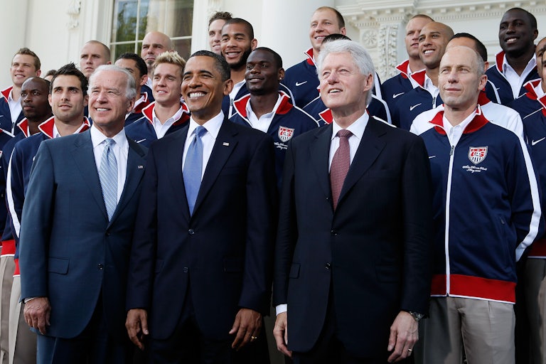 Barack Obama, Joe Biden, and Bill Clinton pose for a picture in front of the U.S. mens World Cup team.