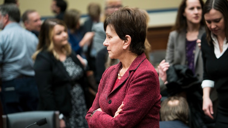 Janet Woodcock stands with arms crossed as people mill about.