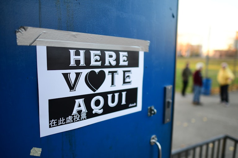 A sign says "Here VOTE Aqui." The "o" in Vote is a heart.