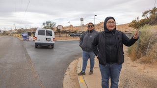 Two Native women stand on the sidewalk as a white fan is seen in the background