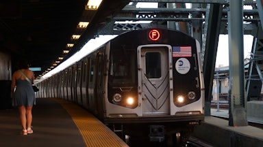 A person in a dress waits as a train bearing an American flag approaches the platform.