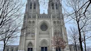 This picture shows Washington National Cathedral in winter, surrounded by bare trees and a thin dusting of snow on the ground.